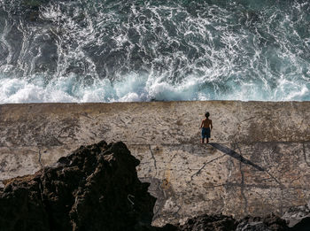 High angle view of man standing on rock by sea