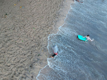 High angle view of mother walking towards daughter surfing in sea