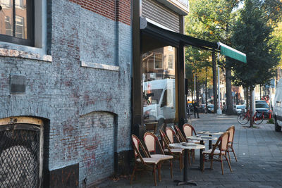 Empty chairs and tables at sidewalk cafe by buildings in city