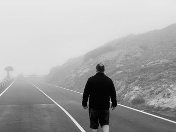 Rear view of man walking on road against sky during foggy weather