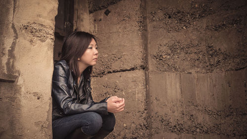 Side view of a young woman sitting against wall