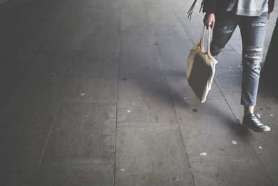 Low section of woman walking with bag on footpath