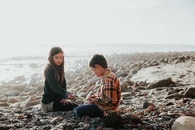 People sitting on rocks at beach against sky