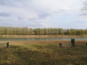 Empty bench on field by lake against sky