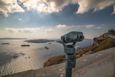 Coin-operated binoculars amidst retaining wall by sea against cloudy sky
