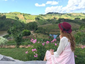 Rear view of woman looking at view while sitting on retaining wall against sky