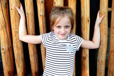 Portrait of smiling girl standing against wooden posts