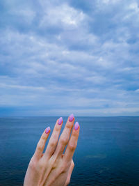 Woman hand by sea against sky