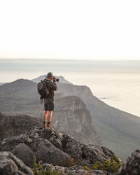 Man photographing sea on rocky mountains against clear sky