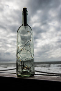 Glass of water on table by sea against sky