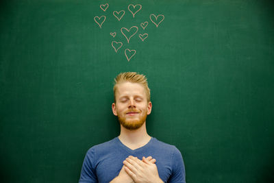 Smiling young man gesturing with heart shapes on blackboard