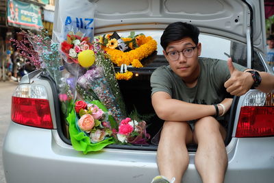 Portrait of young man with bouquet sitting in car trunk