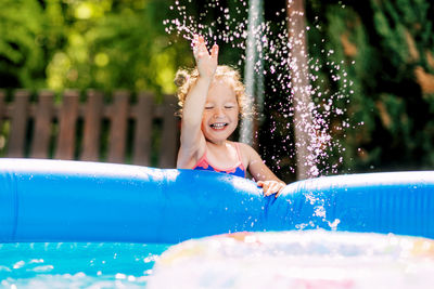 A cute baby girl splashes water in an inflatable pool in the garden and laughs. summer, water