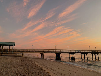 Pier on beach against sky during sunset