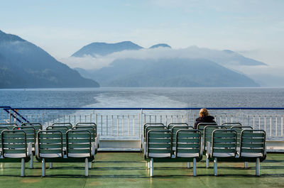 Rear view of woman sitting on chair at ship against mountains