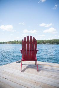 Red chair on floor by lake against sky