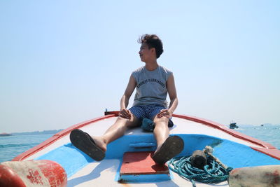 Young man sitting in sea against clear sky