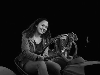 Portrait of smiling young woman driving tractor against black background