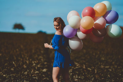 Side view of woman holding colorful balloons while standing on land