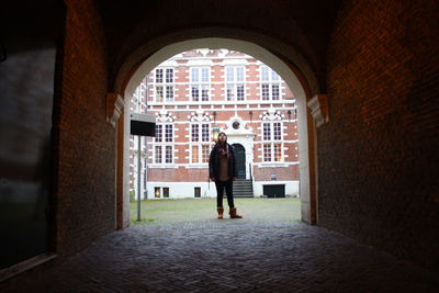 Full length of woman standing on footpath seen through archway