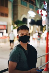 Portrait of young man wearing mask standing on street in city at night