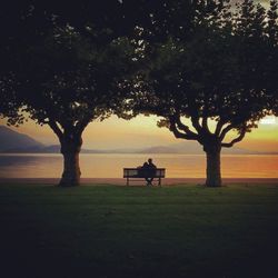 Rear view of couple sitting on bench by lake during sunset