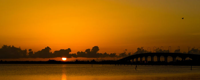 Silhouette bridge over river against orange sky