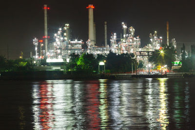 Illuminated factory by river against sky at night