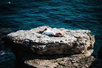 Young woman lying down by sea on rock