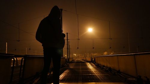 Rear view of silhouette man walking on illuminated street light at night