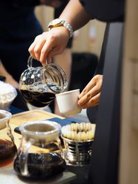 Cropped image of person pouring tea cup on table