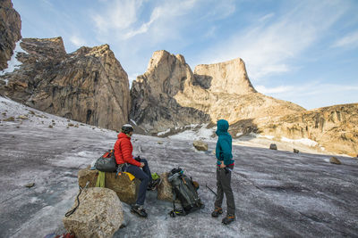 People on rocks by mountains against sky