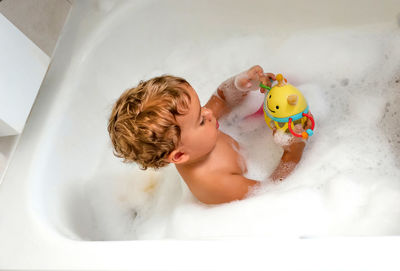 Child bathing in tub at home with foam