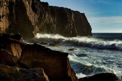 Waves splashing on rocks by sea against sky