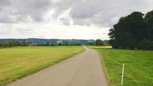 Empty road amidst field against sky