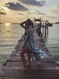 Full length of woman standing by sea on pier over during sunset