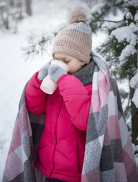 Little girl wrapped in a blanket drinking tea in the winter forest