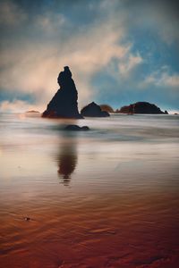 Silhouette rock formation in sea against sky during sunset