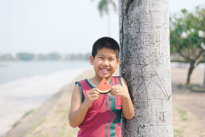 Portrait of smiling boy eating watermelon by tree