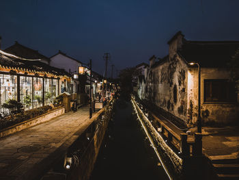 Illuminated street amidst buildings against sky at night