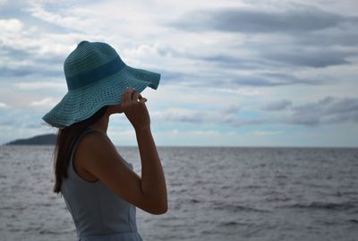 Side view of woman wearing hat standing against sea