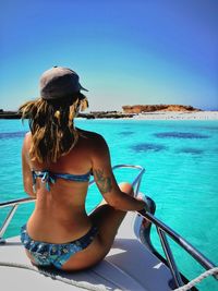Rear view of woman wearing bikini while sitting in yacht against clear blue sky