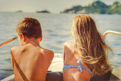 Rear view of siblings sitting in boat at sea