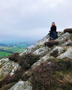 Woman sitting on mountain against cloudy sky