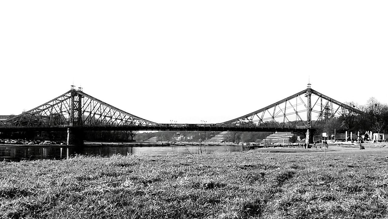 clear sky, copy space, bridge - man made structure, grass, connection, built structure, architecture, transportation, bridge, engineering, outdoors, day, tree, nature, field, river, tranquility, growth, incidental people, plant