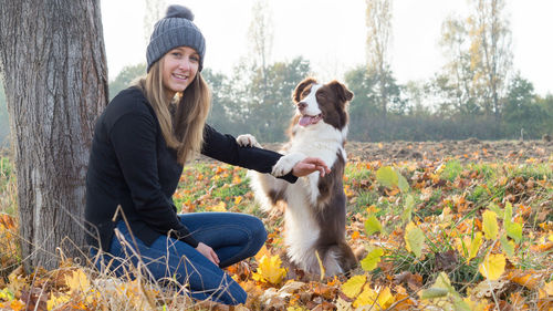 Portrait of woman with dog against tree trunk 