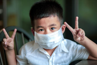 Portrait of boy wearing mask gesturing sitting on chair