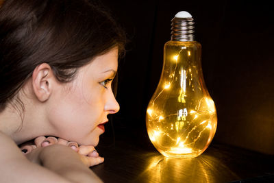 Close-up portrait of girl looking at illuminated light bulb
