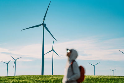 Person standing by wind turbine in agricultural field against clear blue sky