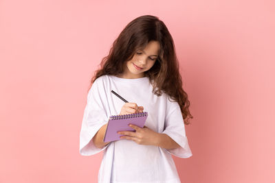 Young woman holding gift against pink background